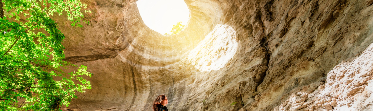 A young woman is standing underground with a view of a huge hole in the rock